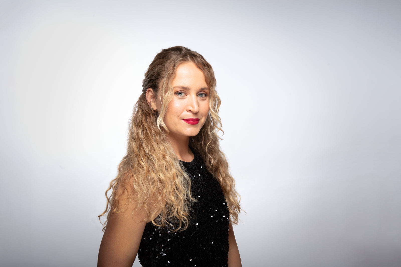 woman in front of a grayscale background styled with a half up half down wavy hairstyle