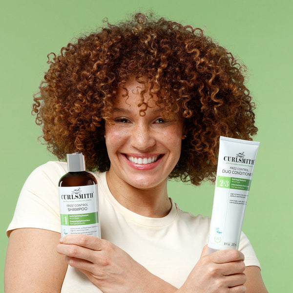 Woman holding Curlsmith hair care products against a green background