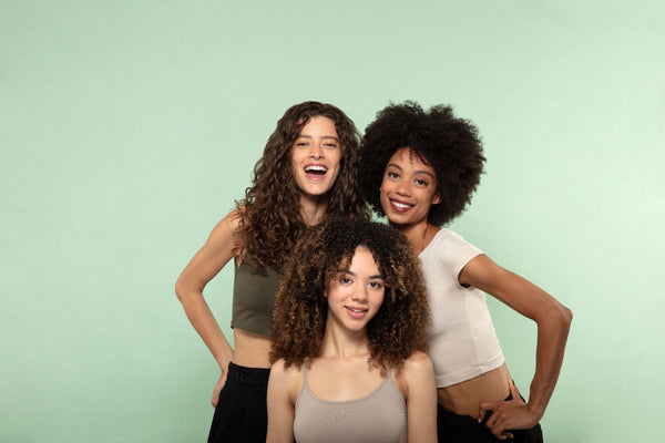 Three curly haired women in front of green background