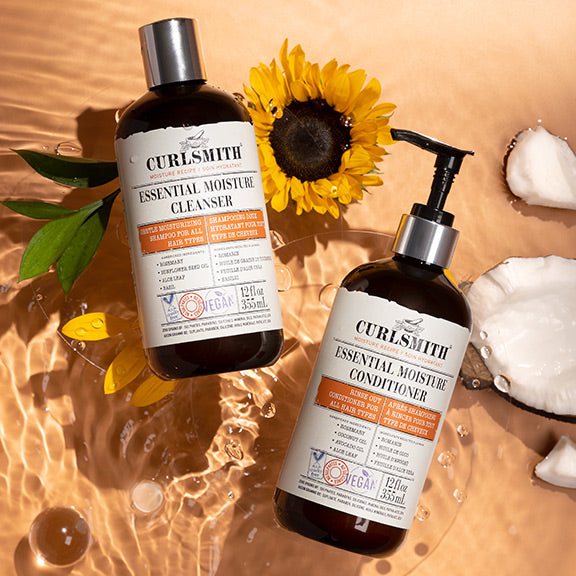 Two bottles of Curlsmith hair care products with a sunflower and leaves on a water surface.