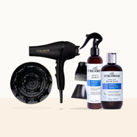 Curlsmith hair styling kit including a black hair dryer with diffuser attachment, black concentrator nozzle, brown bottles of Miracle Shield and Regrowth Hair Salve, and a black comb attachment, arranged on a light beige background.