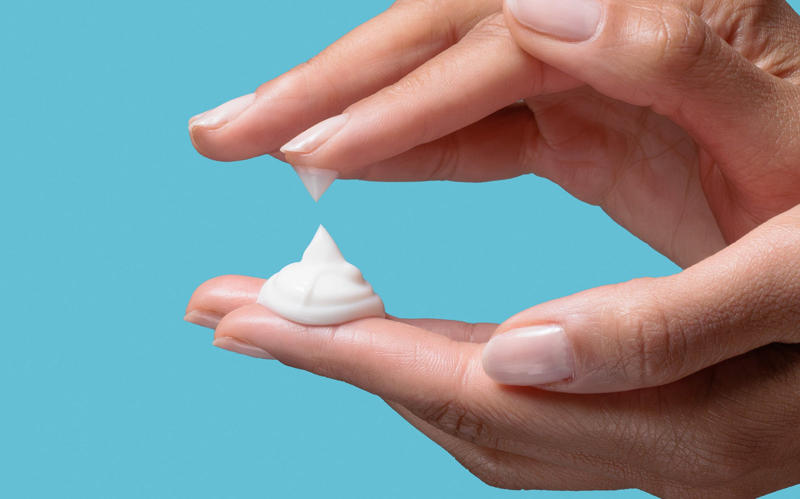 Hand holding a small amount of white cream against a blue background